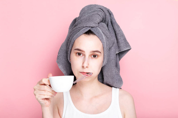 Tired and sleepy young girl drinks coffee and brushes her teeth at same time on pink background. Concept early morning rises, morning routine - Φωτογραφία, εικόνα