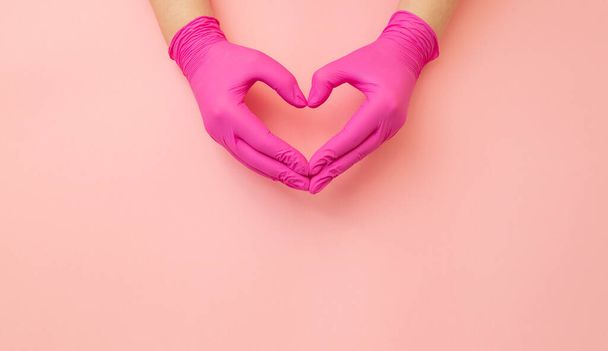 Female hands in medical red gloves made in shape of heart on pink background. Banner with copy space for info about thanks to the doctors. - Photo, image