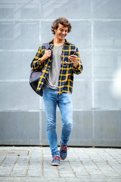 Full length portrait happy travel man walking with cellphone and earphones - Photo, image
