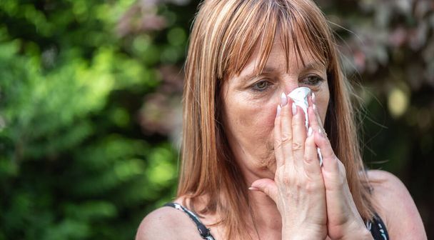 Mature woman blowing her nose outdoors - Photo, Image