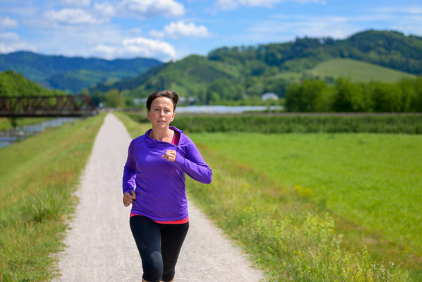 Mulher correndo no campo na primavera se aproximando da câmera com um olhar de determinação em um conceito saudável de estilo de vida ao ar livre
 - Foto, Imagem