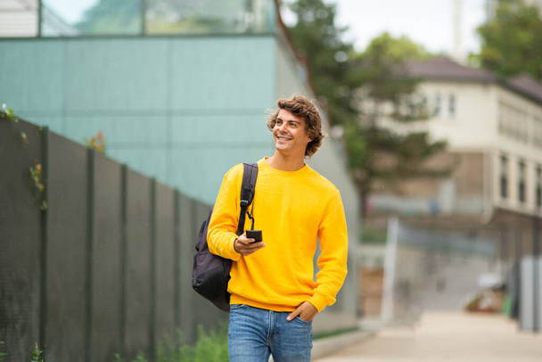 Porträt attraktiver junger Mann geht mit Tasche und Handy  - Foto, Bild