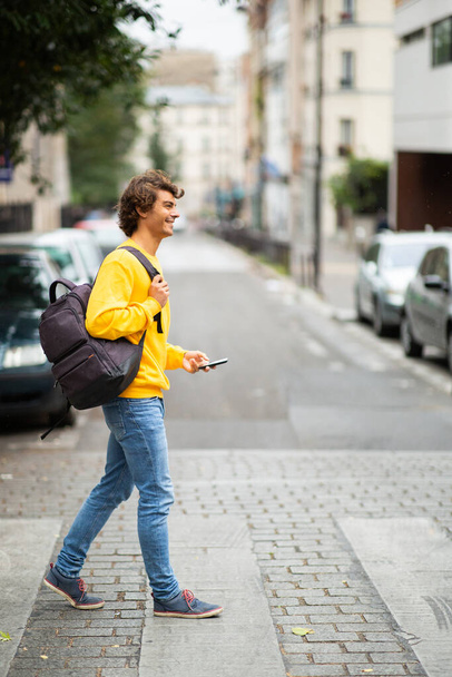 Profil pleine longueur portrait jeune homme avec sac et téléphone portable traversant la rue
 - Photo, image