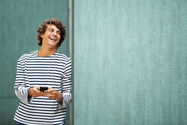 Retrato legal jovem rindo com telefone celular por fundo verde
 - Foto, Imagem