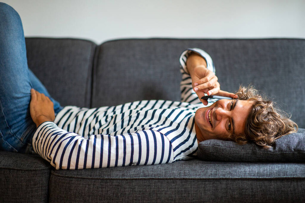 Portrait jeune homme heureux se détendre sur le canapé parler avec téléphone mobile
  - Photo, image