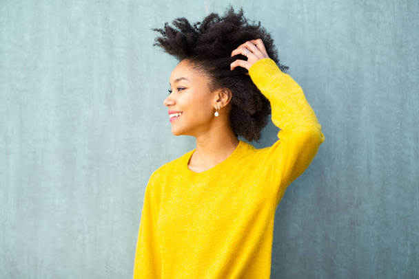 Portret uśmiechnięty młoda czarna kobieta pozowanie z ręką we włosach odwracając wzrok - Zdjęcie, obraz