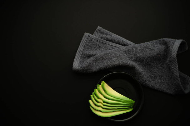 Affettato fette di avocado mature su un piatto nero su uno sfondo scuro. Grassi vegetali e acidi omega per una colazione equilibrata - Foto, immagini