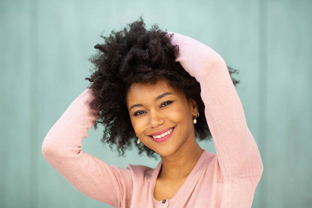 Nahaufnahme Porträt lächelnde junge schwarze Frau mit Händen hinter dem Kopf vor grünem Hintergrund  - Foto, Bild