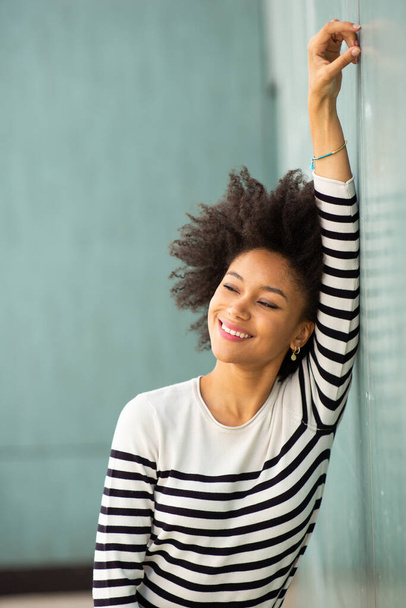 portrait young black woman leaning against wall with arm raised - Photo, Image