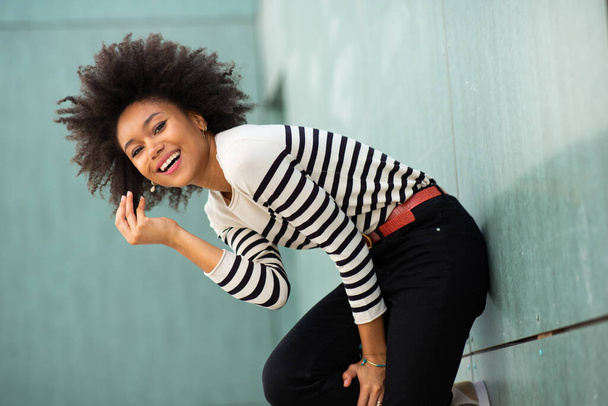 Side portrait laughing young african american woman with afro hair leaning against wall - Foto, Bild