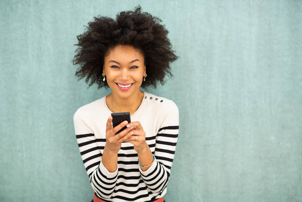 Πορτρέτο ευτυχισμένη νεαρή Αφροαμερικανή γυναίκα κρατώντας κινητό τηλέφωνο από πράσινο φόντο - Φωτογραφία, εικόνα