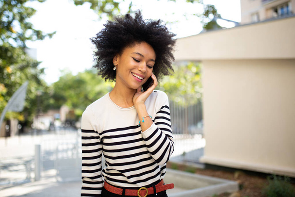 Ritratto sorridente giovane donna nera che parla con il cellulare fuori
 - Foto, immagini