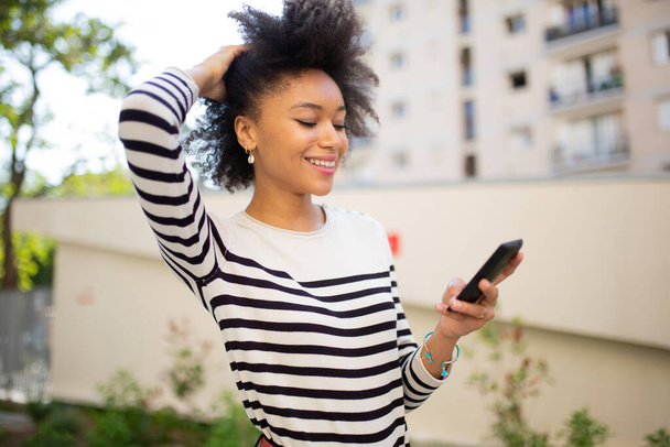 Side portrait smiling young black woman looking at smartphone outside - 写真・画像