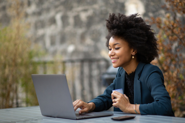 Retrato de mujer de negocios afroamericana sentada afuera con computadora portátil
 - Foto, Imagen