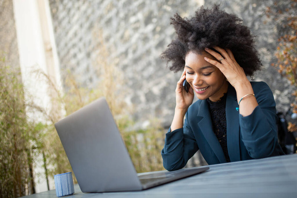 Закрыть портрет улыбающейся деловой женщины, работающей с ноутбуком и мобильным телефоном
 - Фото, изображение