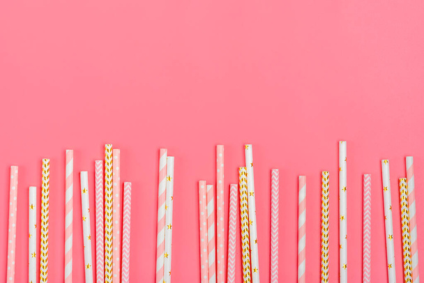 Drinking paper straws for party with golden, white, pink stripes on pink pastel background with copy space. Top view of colorful paper disposable eco - friendly straws for summer cocktails. Flat lay. - Photo, Image