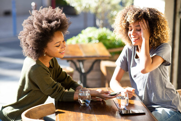 Retrato feliz joven afroamericano mujeres sentadas en la cafetería al aire libre con teléfono celular
 - Foto, imagen