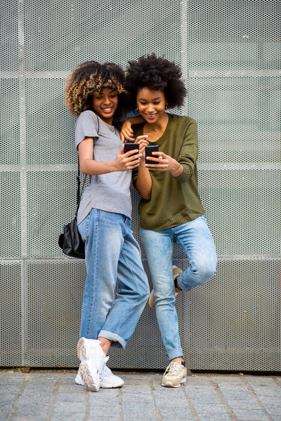 Full body portrait two happy black young women with cellphone  - Photo, Image