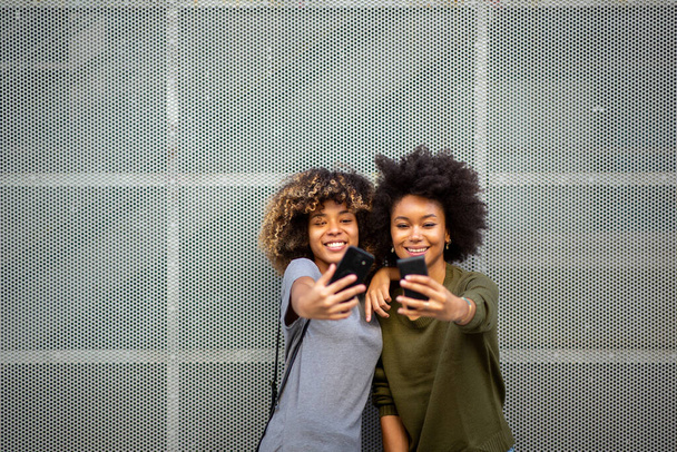 muotokuva kaksi onnellista nuorta mustaa naista, jotka ottavat selfien matkapuhelimilla
  - Valokuva, kuva