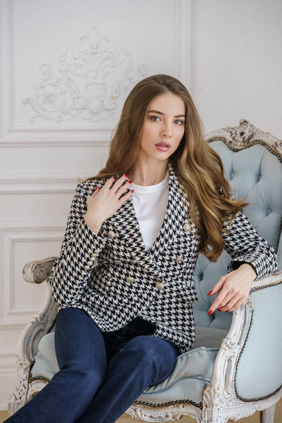 Portrait of beautiful young woman in casual clothes sitting in armchair at luxury apartments interior - Valokuva, kuva