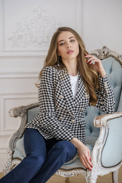 Portrait of beautiful young woman in casual clothes sitting in armchair at luxury apartments interior - Foto, Bild