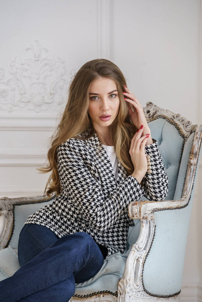 Portrait of beautiful young woman in casual clothes sitting in armchair at luxury apartments interior - Fotografie, Obrázek
