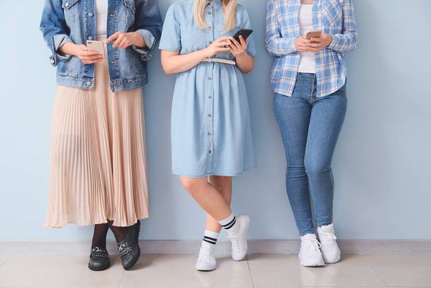 Naiset matkapuhelimet lähellä väriseinää
 - Valokuva, kuva