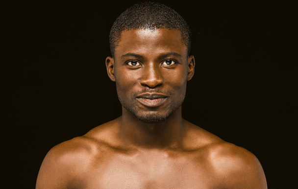 Nude smiling African macho man posing on black background, portrait of an attractive African american man smiling slightly while looking at the camera. Toned image - Photo, Image