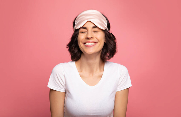 Bright morning smile. Close-up photo of a lovely girl in a face mask and pajamas, who is smiling with her eyes closed. - Photo, Image