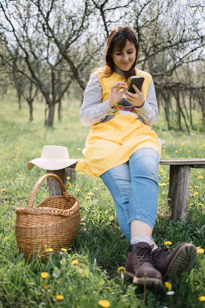 Lady sitting on bench with basket and sun hat - Фото, зображення