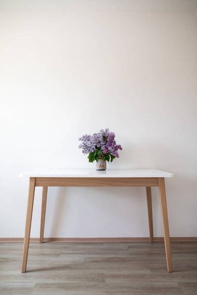On a white table is a vase of lilac flowers. Image is used for interior design. Interior Design. A bouquet of lilacs. White table in the frame. Space for tex. Art object. - Fotoğraf, Görsel