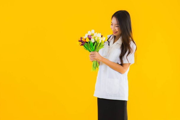 retrato hermosa joven asiático mujer mostrar colorido flor en amarillo aislado fondo
 - Foto, Imagen