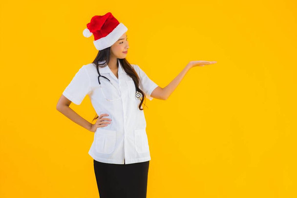Portret piękny młody Azji lekarz kobieta nosić Boże Narodzenie lub Santa kapelusz na żółtym odizolowanym tle - Zdjęcie, obraz