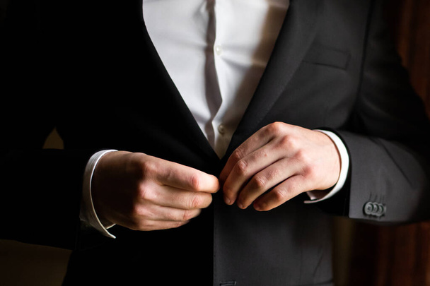 L'uomo d'affari in giacca e cravatta si chiude la giacca. Vestito casual intelligente. Un uomo che si prepara per il lavoro. sposo in una giacca, lo sposo fissa la giacca. La mattina dello sposo, le tasse dello sposo
 - Foto, immagini