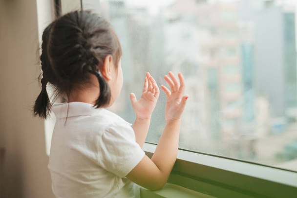 A lovely kid girl sitting and looking outside trough the window - Photo, Image