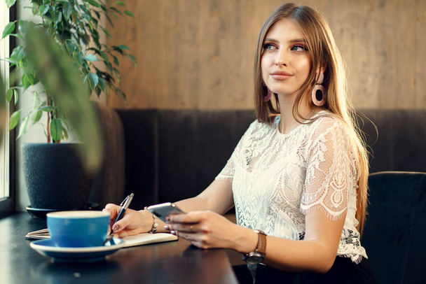 Young business woman sitting at the table in a coffee shop and making notes - Foto, afbeelding