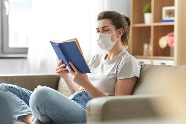 sick woman in medical mask reading book at home - Fotó, kép