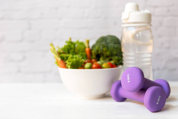 Diet Health Food und Lifestyle-Gesundheitskonzept. Sportgeräte Workout und Fitness-Studio Hintergrund mit frischem Salat für Fitness-Stil. Konzept eines gesunden Lebensstils - Foto, Bild