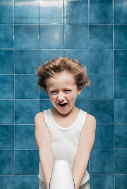 A child in the bathroom drying his hair with a hairdryer, gesturing. - Photo, image