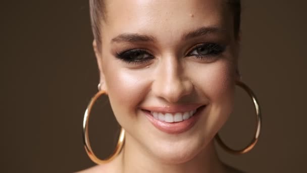 A close-up view of a pretty nice young half-naked woman wearing stylish earrings is laughing isolated over the beige background in studio - Footage, Video