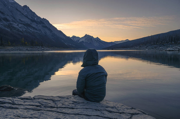 İnsan gezgin sabah Medicine Gölü 'nde kayanın üzerinde oturuyor Jasper Ulusal Parkı, Kanada - Fotoğraf, Görsel