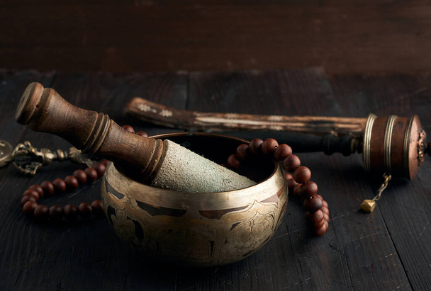Tibetaanse zingende koperen kom met een houten klepel op een bruine houten tafel, voorwerpen voor meditatie en alternatieve geneeskunde, close up - Foto, afbeelding