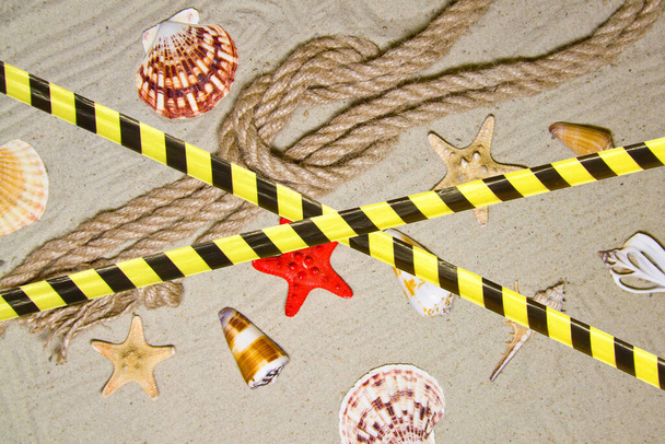Barrièreband - quarantaine, isolatie, toegangsverbod. Zeeschelpen en nautische touw decoratie op zand achtergrond met rood speelgoed schip. - Foto, afbeelding