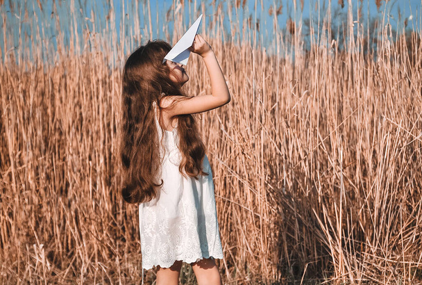 Little cute girl with paper plane has fun outdoors. - Photo, Image