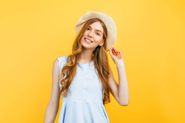 Portrait of a cheerful young girl in a summer hat, dressed in summer clothes, smiling on an isolated yellow background - Photo, image