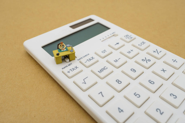 Миниатюрные люди платят на калькуляторе фиксированный доход (TAX) за год. использование в качестве базовой бизнес-концепции и финансовой концепции с копировальным пространством для текста или дизайна
. - Фото, изображение