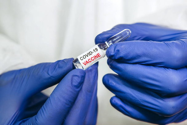 Der Arzt hält ein Reagenzglas mit einem Coronavirus-Impfstoff auf weißem Hintergrund. Impfung covid-19. Pandemie 2020. Die Hände des Arztes stecken in blauen medizinischen Handschuhen. Ein Heilmittel gegen das Virus. - Foto, Bild