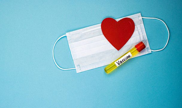an ampoule containing the covid-19 vaccine, invented to prevent the spread of the virus around the world. mask with a red heart on a blue background - Fotoğraf, Görsel