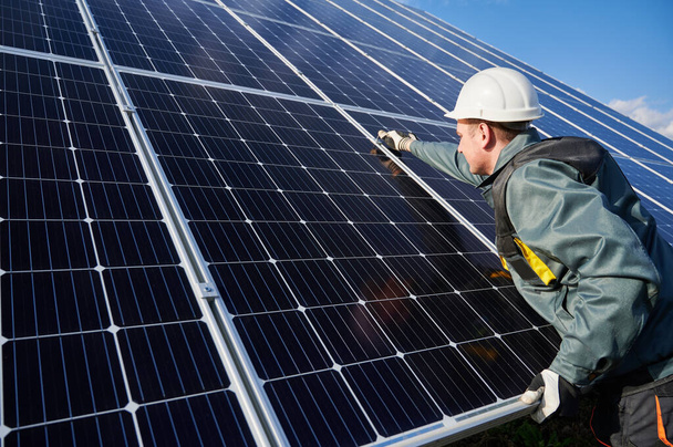 Man technician in safety helmet repairing photovoltaic solar module. Electrician in gloves maintaining solar photovoltaic panel system. Concept of alternative energy and power sustainable resources. - Photo, Image