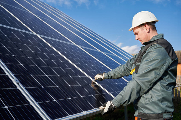 Side view of man technician in safety helmet repairing photovoltaic solar module. Professional electrician worker in gloves maintaining solar photovoltaic panel system. Concept of alternative energy - Photo, Image